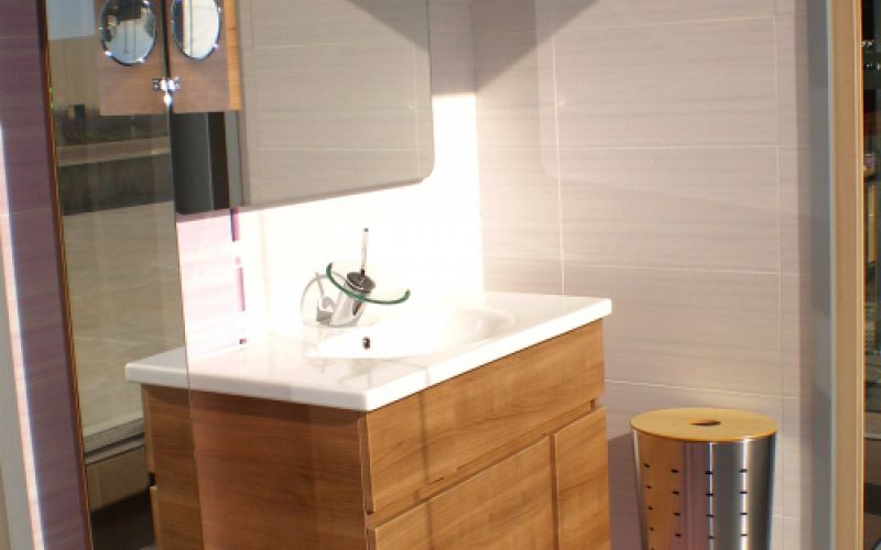 Baño completo en exposición con muebles en madera y sanitarios blancos